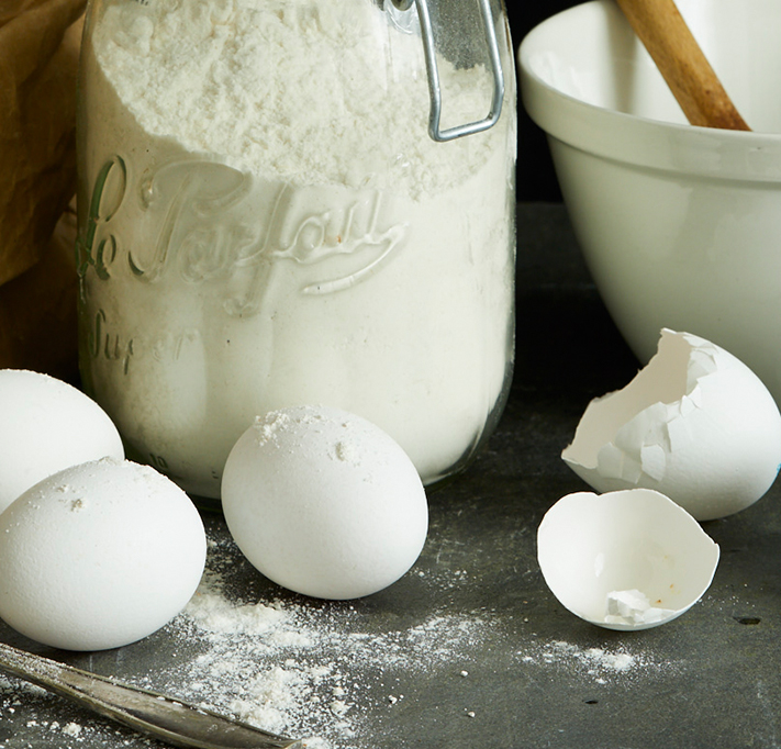 jar of flour and three eggs out for baking, one broken egg