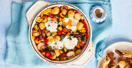 Pan of vegetables, potatoes and eggs made by Alice Liveing, on a blue tablecloth.