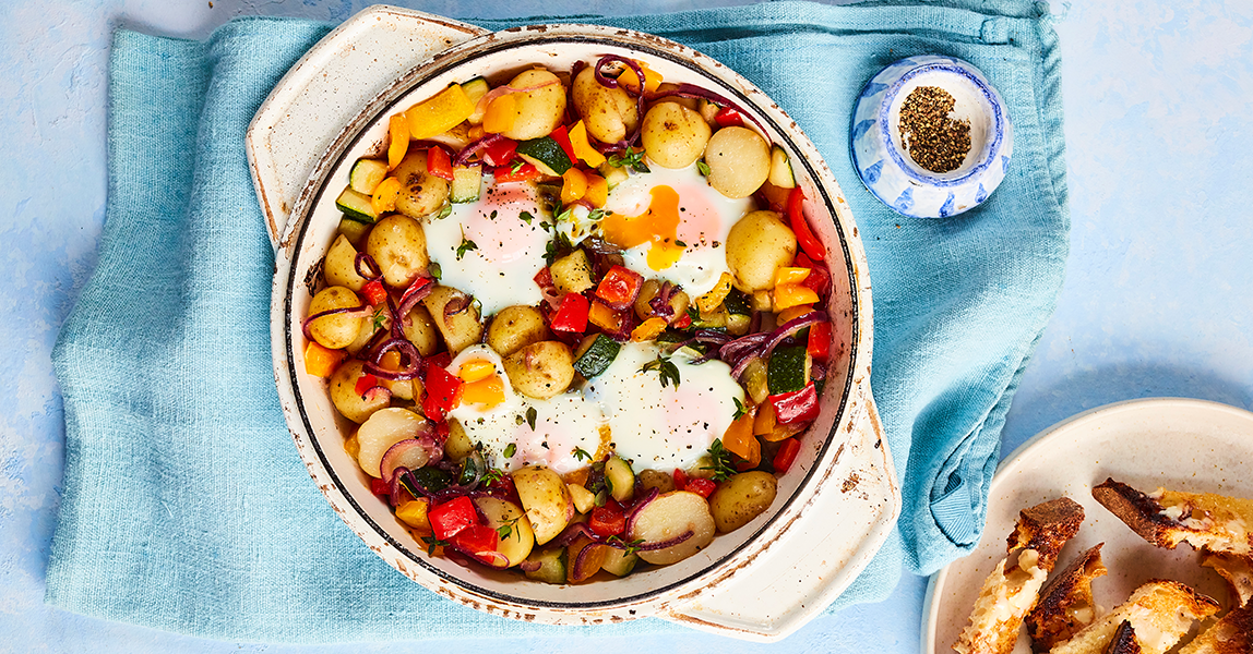 Pan of vegetables, potatoes and eggs made by Alice Liveing, on a blue tablecloth.