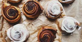 A selection of cinnamon rolls, some iced and others plain, on brown baking parchment.