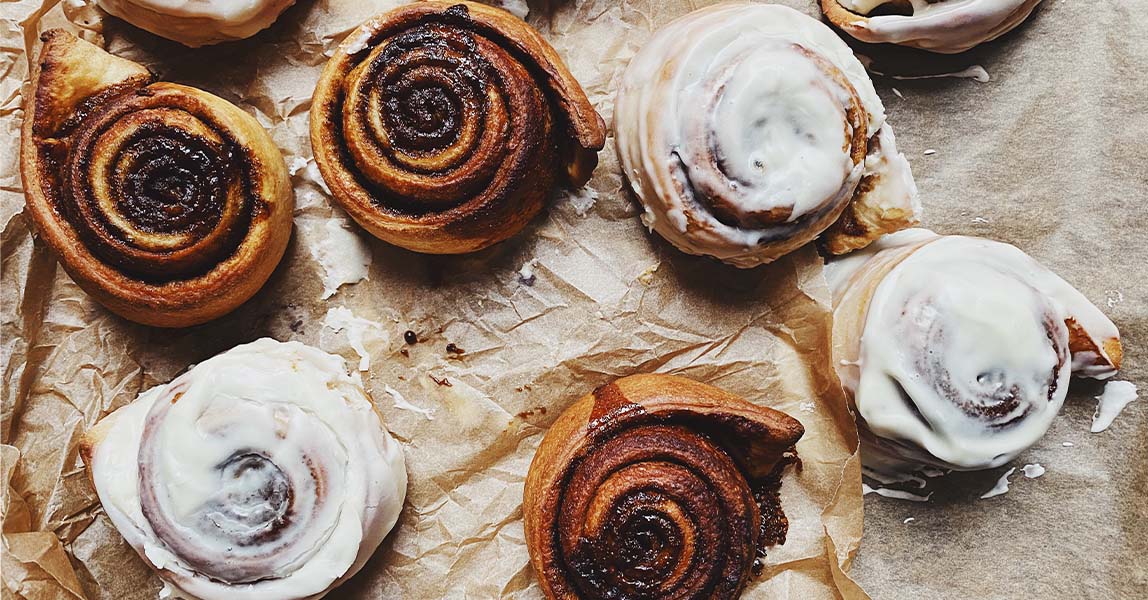 A selection of cinnamon rolls, some iced and others plain, on brown baking parchment.