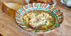 A brown bowl with turquoise stripes around the rim, containing Italian egg soup.