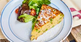 A slice of spaghetti frittata next to a pile of salad leave and chopped tomatoes