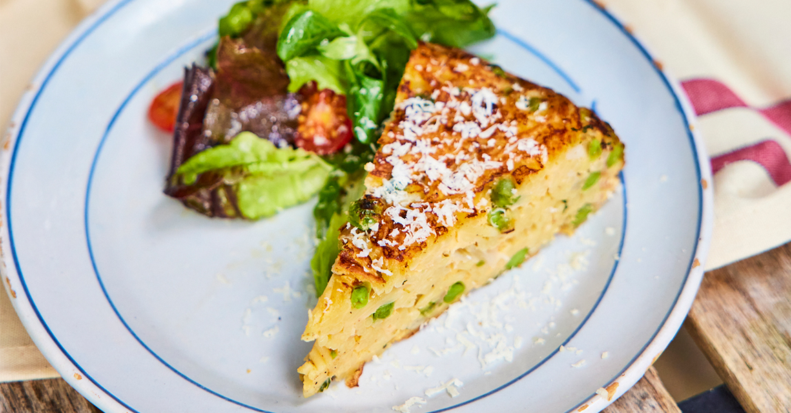 A slice of spaghetti frittata next to a pile of salad leave and chopped tomatoes