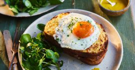 An orange Burford Brown yolk on top of a toasted sandwich, next to green salad.