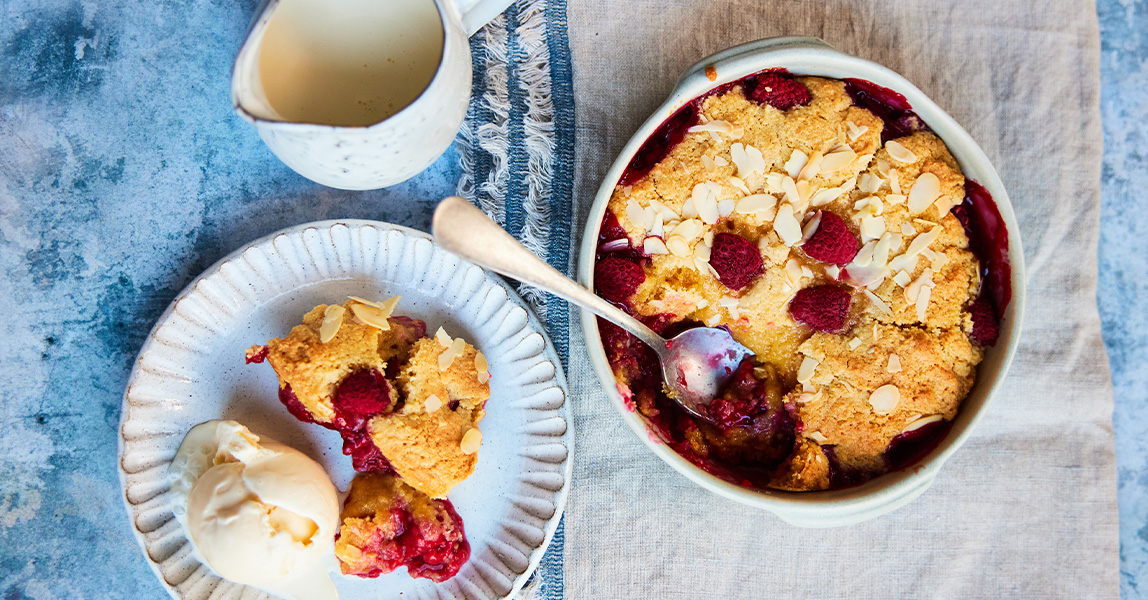 A dish of baked raspberry and almond sponge, next to a plate of the sponge with cream