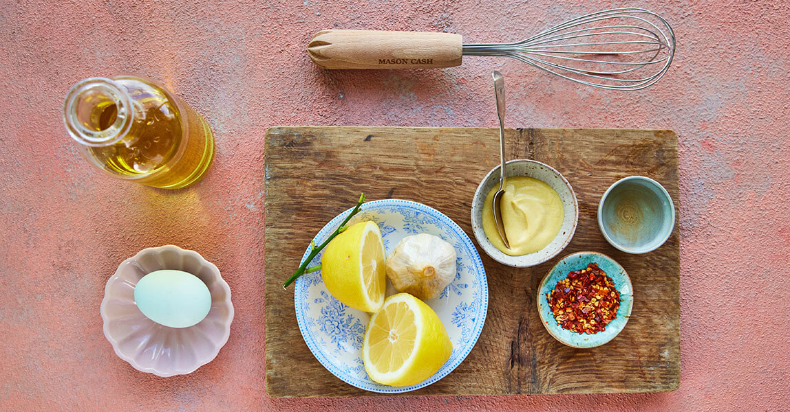 Clarence Court roasted garlic mayonnaise alongside an egg, olive oil and kitchen equipment.