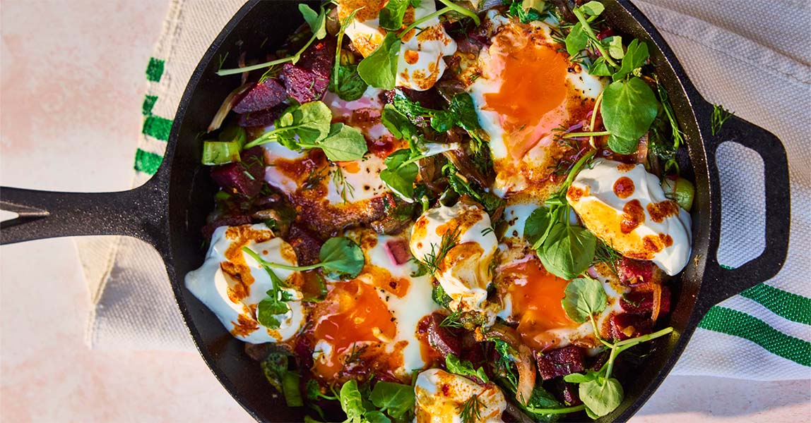 Leek and beetroot eggs sit in a cast iron skillet