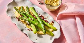 A line of asparagus on an oval plate with a fried Clarence Court egg on top, topped with smoked bacon mayonnaise